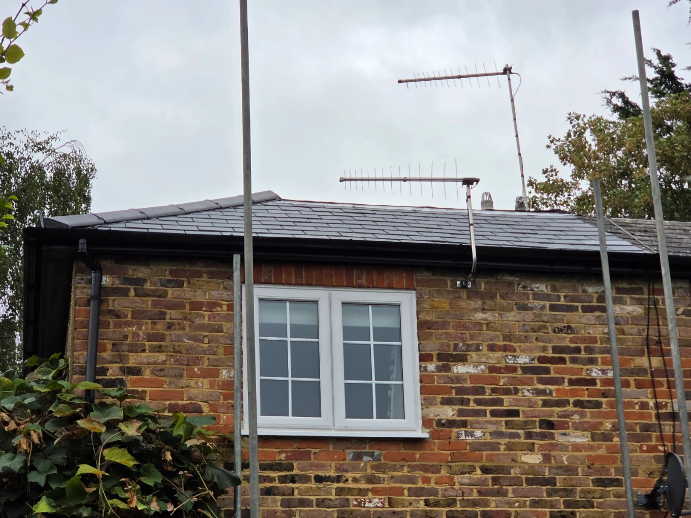 Brick house with black fascia, guttering and downpipe under a dark tiled roof