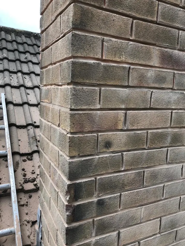 Brick chimney stack with clean, freshly pointed mortar joints beside a tiled roof