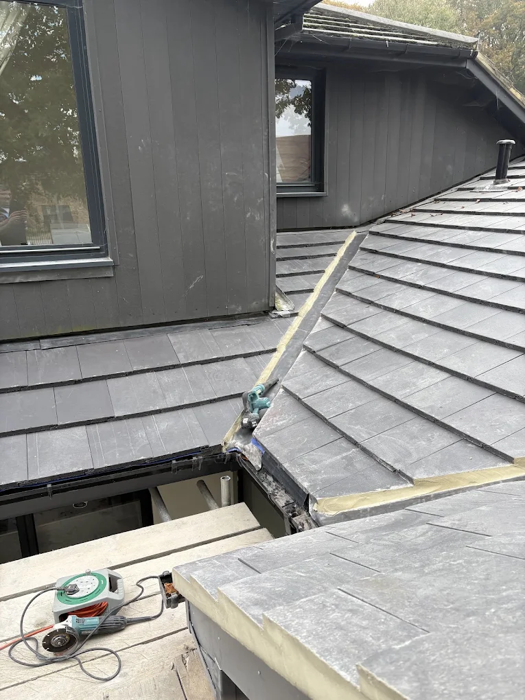 New slate roof on an extension, meeting a dark clad wall, with work still under way