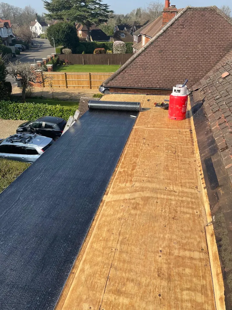 Long flat roof half covered in black felt, the rest bare ply deck, beside a tiled roof