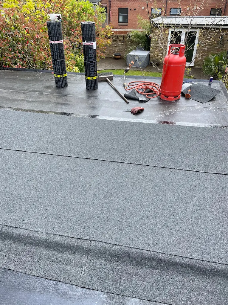 Flat roof finished in torch-on felt, with felt rolls and a gas bottle at the far end