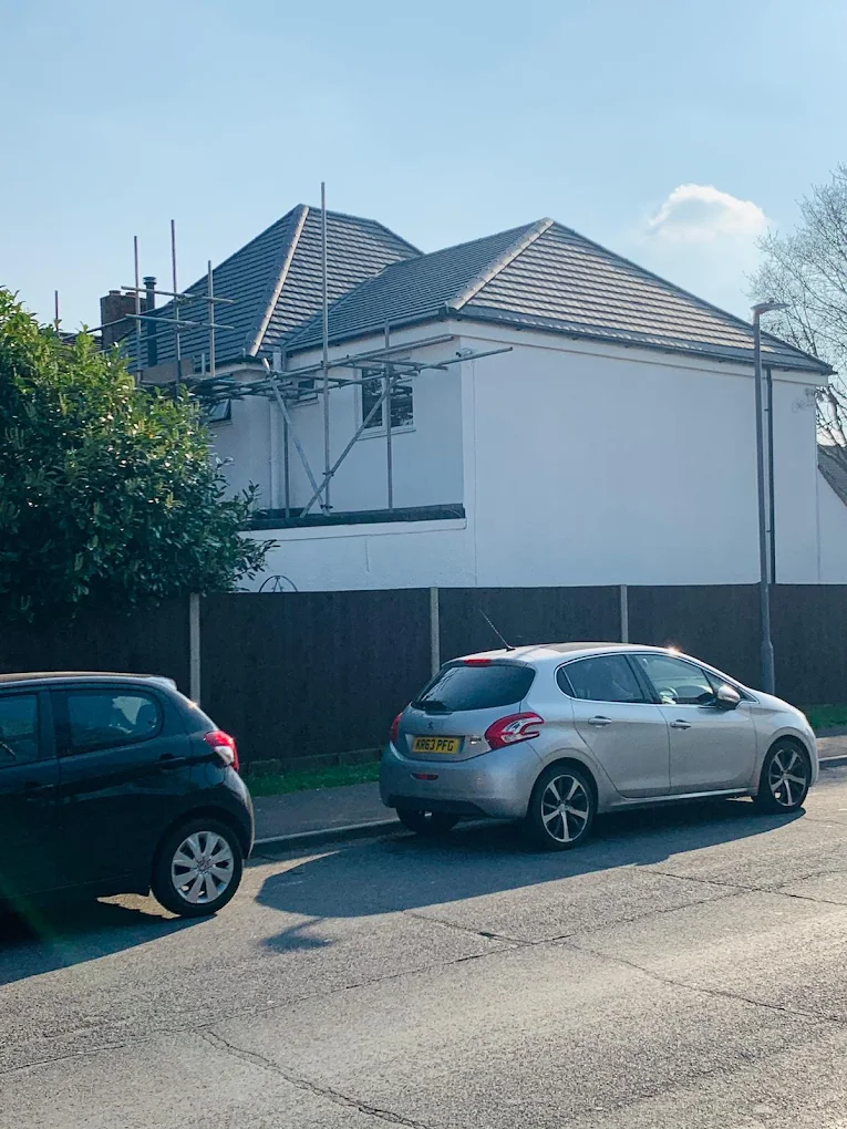 White rendered house with a grey tiled hipped roof and scaffold along one side
