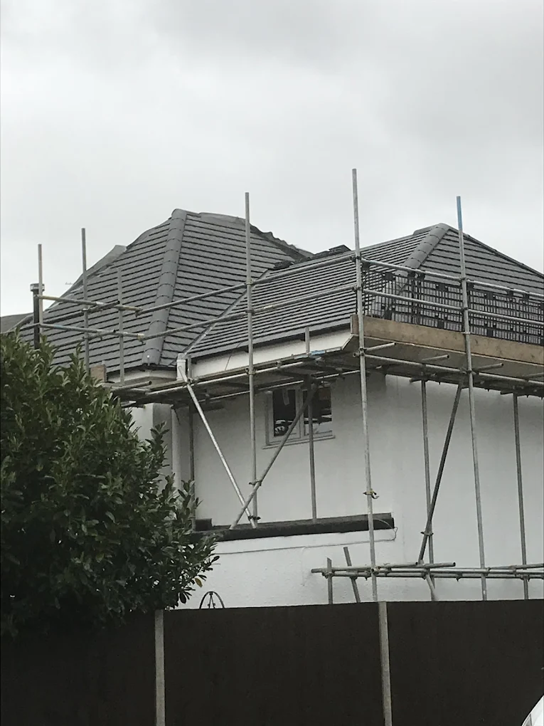 Scaffold around the hipped tiled roof of a white rendered house