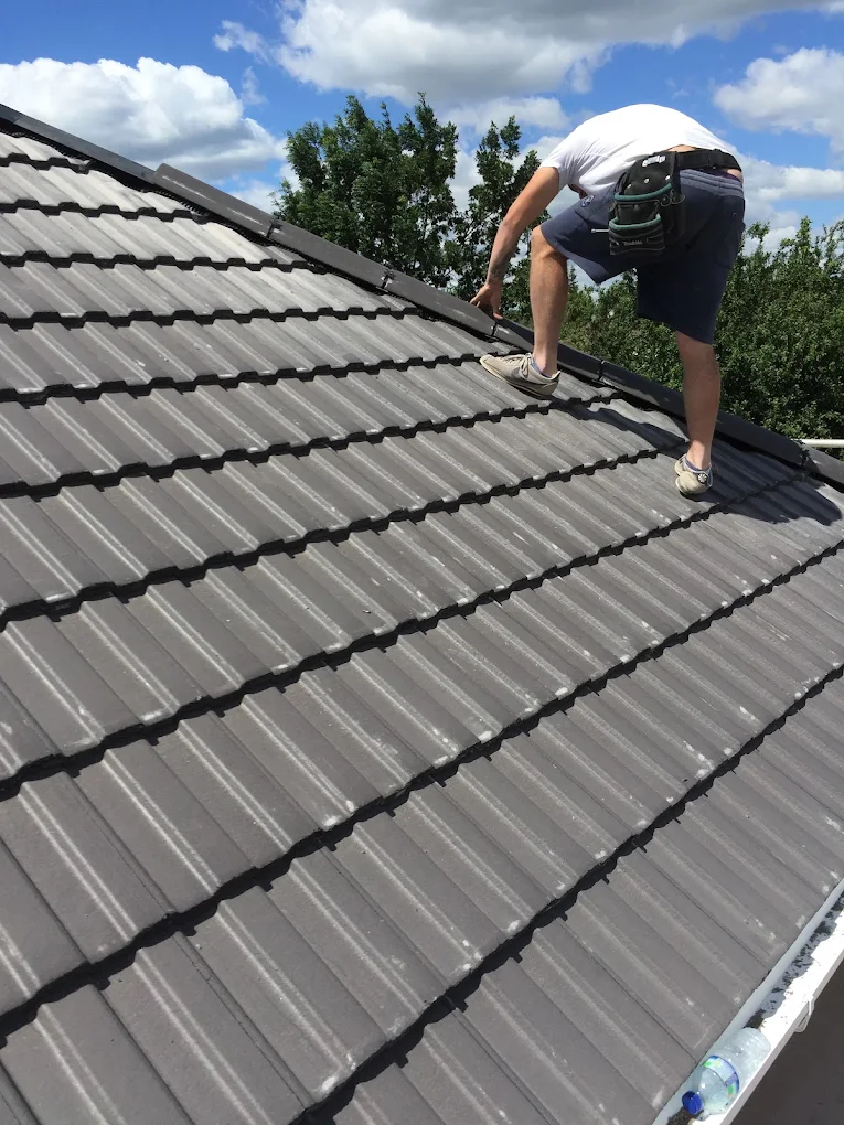 Roofer crouched on a new grey interlocking concrete tile roof under a blue sky