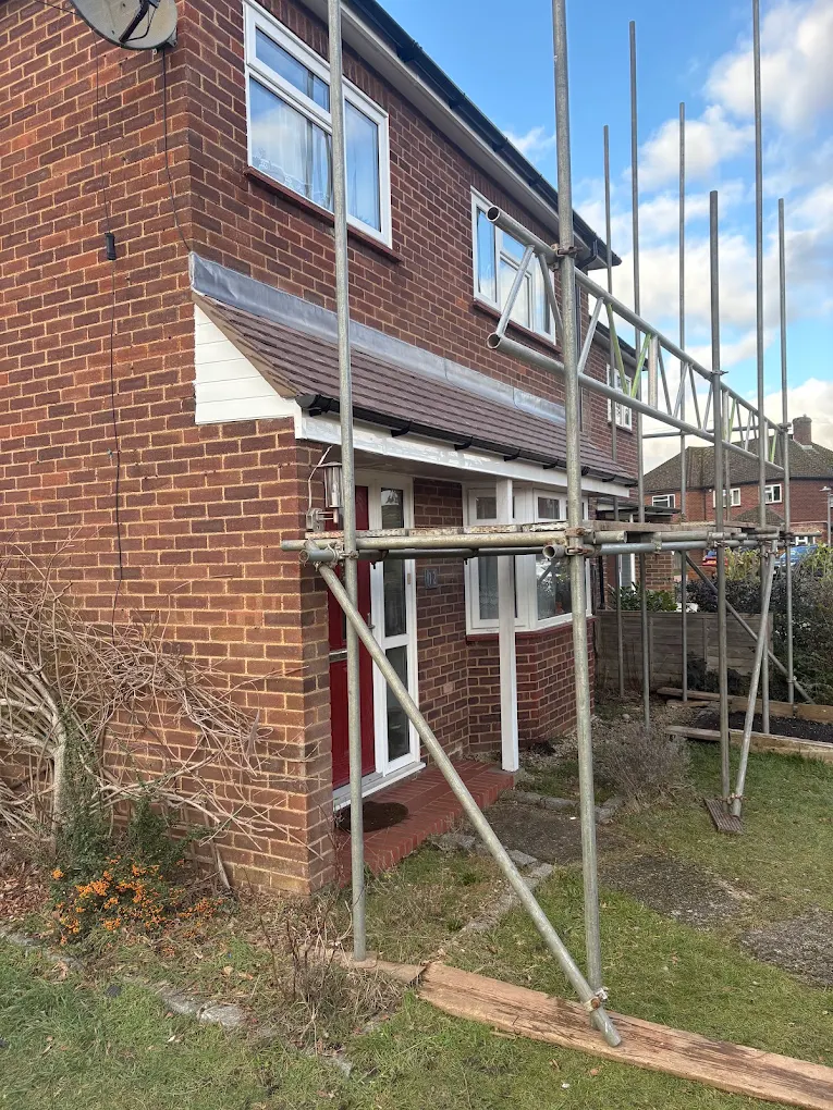 Scaffold against a brick semi-detached house, with a tiled porch canopy over the door