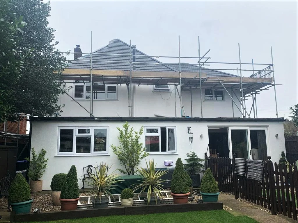 Rear of a white rendered house with scaffold around the roof, garden in front