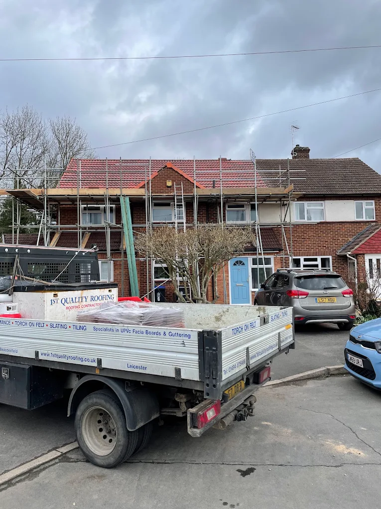 Scaffold round a red tiled roof, with the 1st Quality Roofing truck parked outside