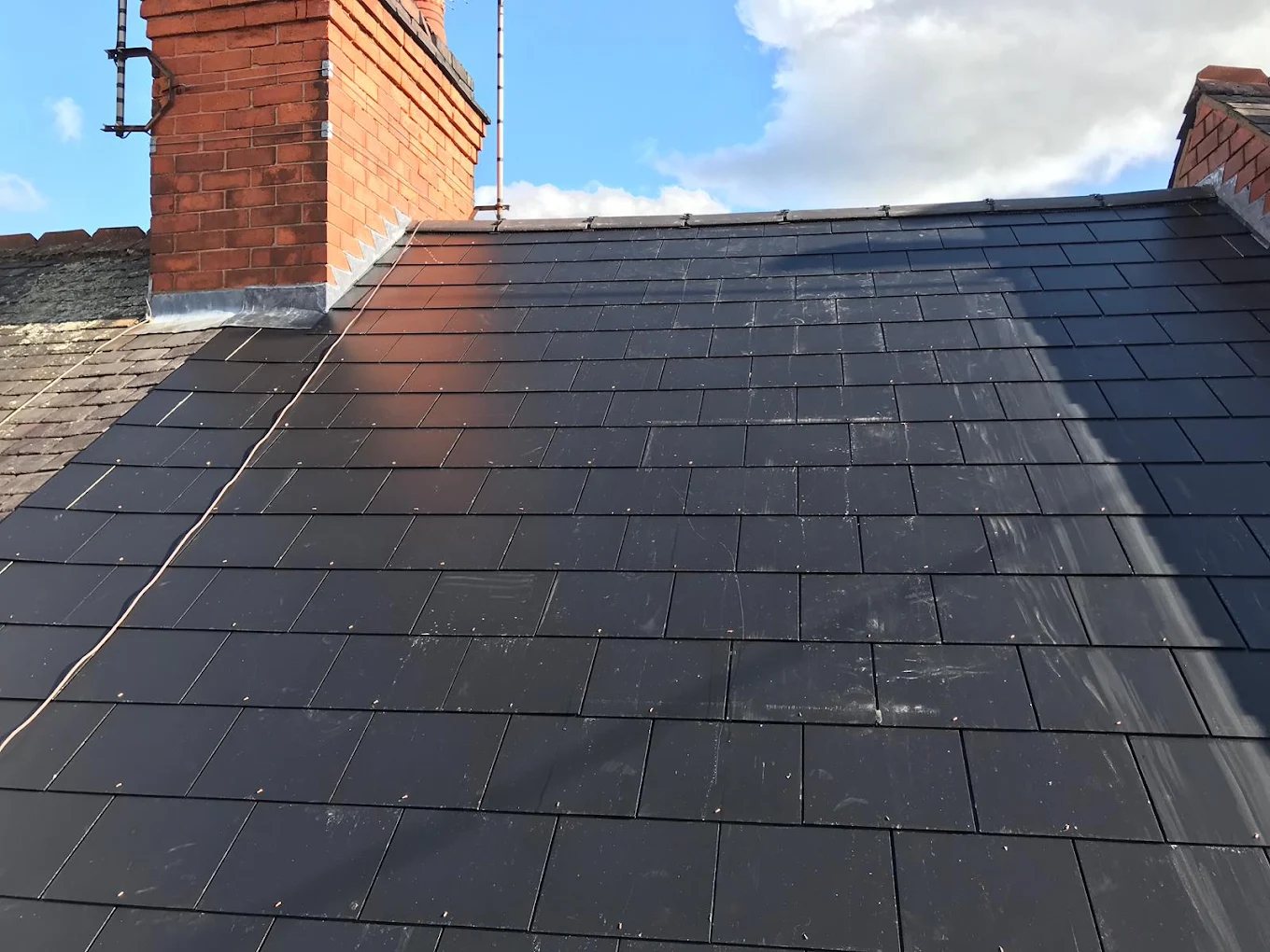 New dark tiled roof running between two brick chimney stacks, lead flashing at the base