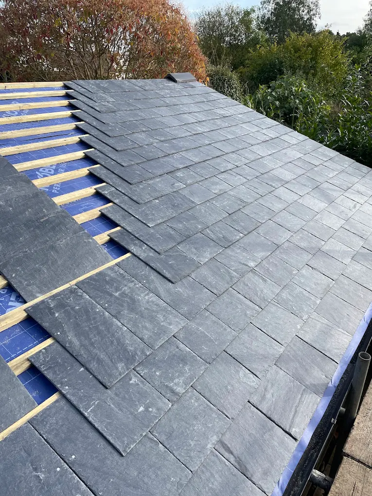 Slate roof part laid, with new battens and blue membrane showing at the edge